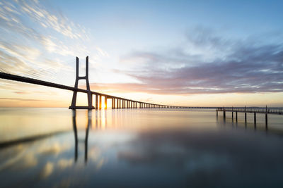 View of suspension bridge over river at sunset