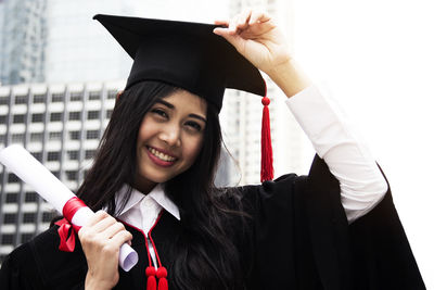 Smiling young woman wearing graduation gown in city