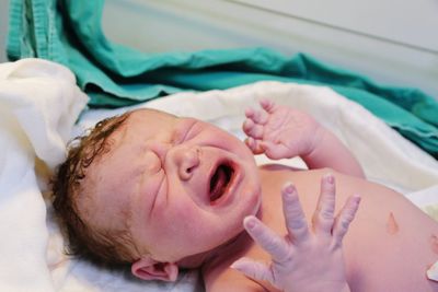 High angle view of newborn baby girl crying while lying on bed in hospital