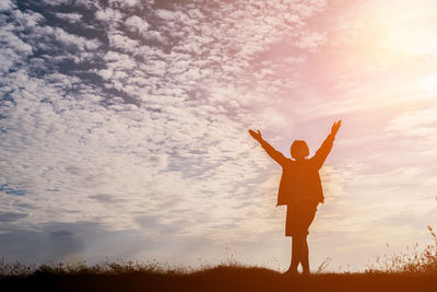 Low angle view of silhouette woman with arms raised standing on land against sky during sunset