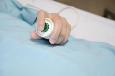 Close-up of human hand on bed holding electric bell at hospital