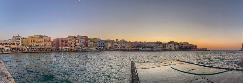 Sea by buildings against clear sky during sunset
