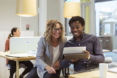 Smiling multi-ethnic coworkers looking at digital tablet in office