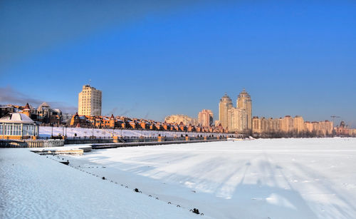 Snow covered buildings in city against clear sky