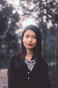 Portrait of young woman standing against trees