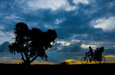 Silhouette people riding bicycle against sky during sunset