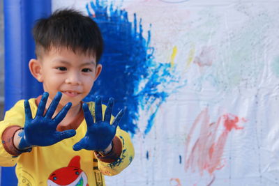 Close-up of cute boy with blue hands against wall