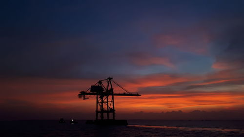 Silhouette crane by sea against sky during sunset