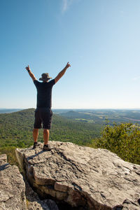 Full length of man with arms raised standing on rock against sky