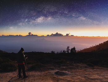 Rear view of man standing on field against sky at night