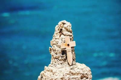 Close-up of cross on rock formation by sea in sunny day