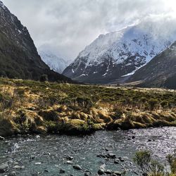Scenic view of stream by snowcapped mountains against sky