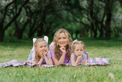 Mom and her daughters are lying on the blanket in a summer park. the family has fun outdoors