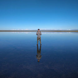 Full length of man standing in sea against clear blue sky