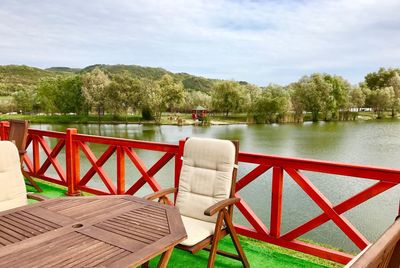 Chairs and table by lake against sky