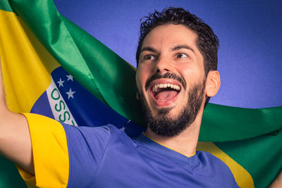 Close-up of happy young man holding national flag while standing against blue background