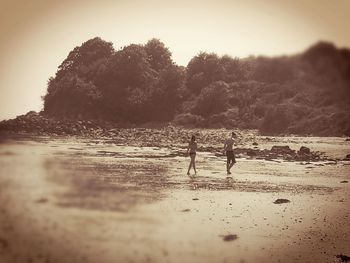 Children standing on beach against sky during sunset