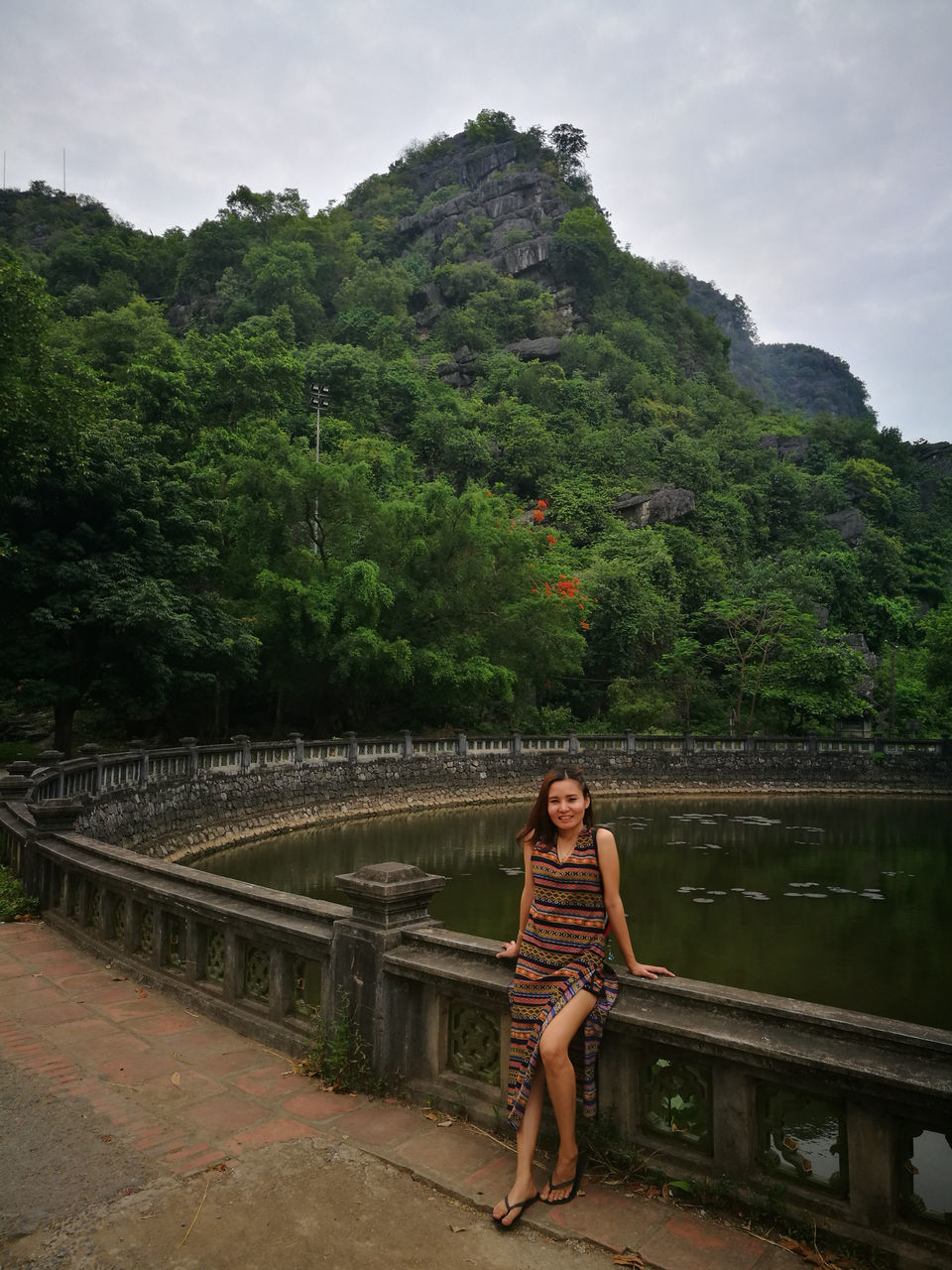 full length, real people, tree, one person, looking at camera, outdoors, young adult, growth, lifestyles, bridge - man made structure, lake, young women, leisure activity, day, water, nature, sitting, portrait, cloud - sky, sky, footbridge, mountain, beauty in nature, retaining wall, architecture