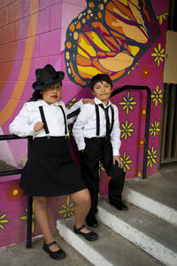 Full length portrait of siblings standing against wall