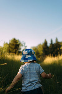 Rear view of boy standing on field against clear sky