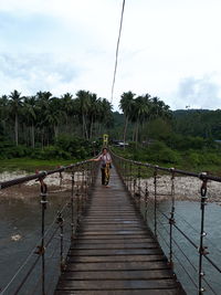 Footbridge amidst trees against sky