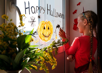 Child painting pumpkin window preparing celebrate halloween kid draws decorates room with paper bats