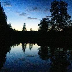 Silhouette trees by lake in forest against sky