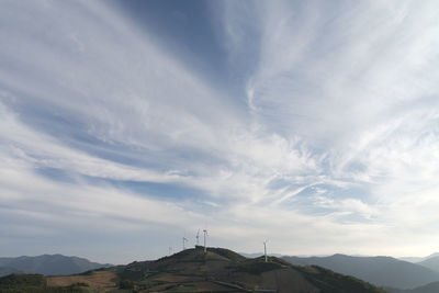 Windmills on landscape against cloudy sky