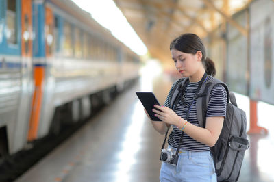 A teen traveler with a tablet and rucksack waiting for a train.