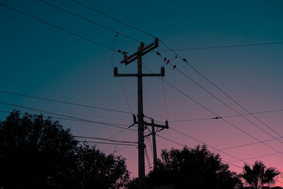 Low angle view of silhouette electricity pylon against sky at sunset