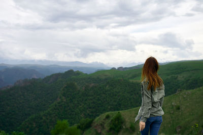 Rear view of woman standing on mountain against sky