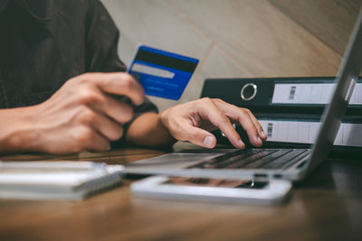 Midsection of businessman using laptop while holding credit card at desk in office