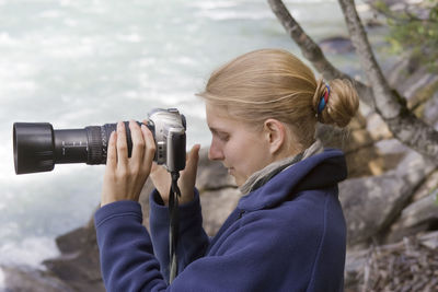 Side view of woman photographing with camera outdoors
