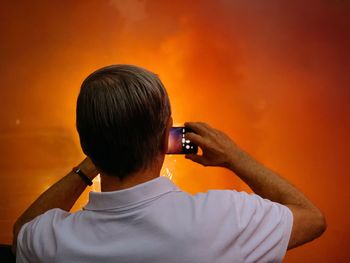 Rear view of man photographing orange camera