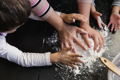 Close up view of woman's and boy's hands mixing dough on a table at home