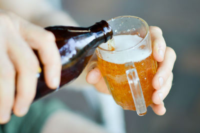 Cropped hand of man pouring beer in glass from bottle