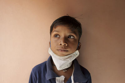 Close-up of boy wearing flu mask standing against wall