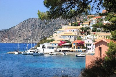 Sailboats moored on sea by buildings against sky