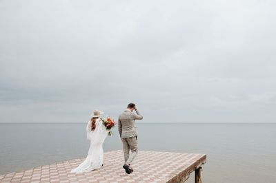 Bride and bridegroom walking on pier in sea during wedding ceremony