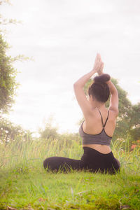 Rear view of young woman in grass against sky