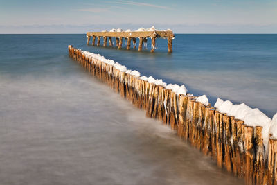 Snow on wooden posts in sea against sky
