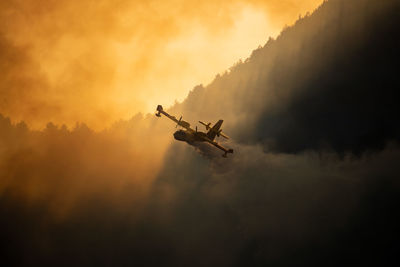 Low angle view of airplane flying against sky during sunset