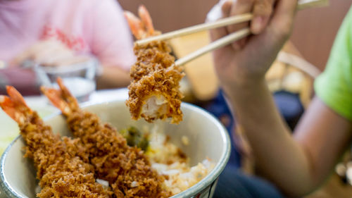 Cropped hand of person holding katsu with chopsticks over bowl