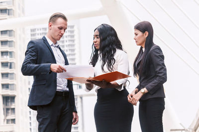 Business people discussing over file while standing against building