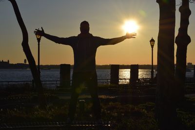 Silhouette of man standing at lakeside at sunset