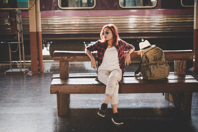 Full length of young woman sitting on bench at railroad station