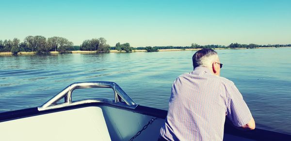 Rear view of man looking at lake against clear sky