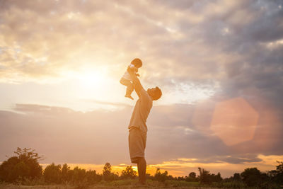 Side view of boy standing on field against sky during sunset