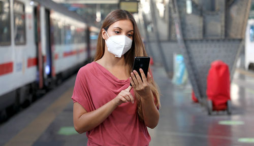 Woman using smartphone while standing at railroad station