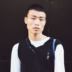 Portrait of young man standing against black background